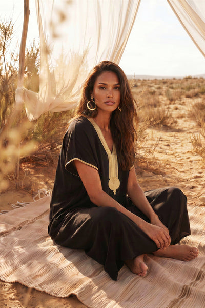 Woman in a black and gold outfit sitting on a blanket in a desert setting