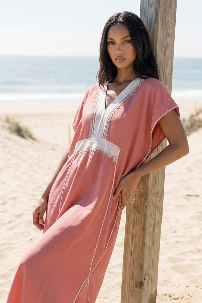 Woman in a pink dress standing on a sandy beach with ocean view