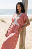 Woman in a pink dress standing on a sandy beach with ocean view
